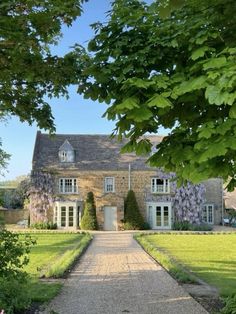 a large house that is in the middle of some grass and trees with purple flowers on it