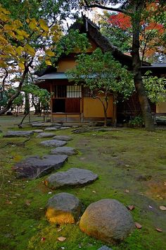 a small house in the middle of a grassy area with rocks and trees around it