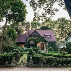 a large house surrounded by lush green trees and bushes in front of a gated driveway