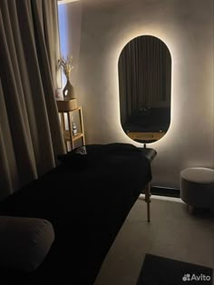 a dimly lit room with a round mirror and black bed in the foreground, along with white drapes on the walls