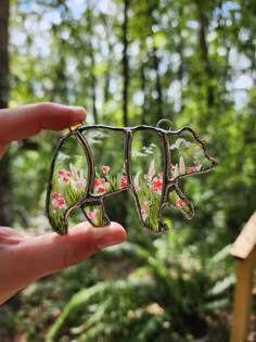 a hand holding up a piece of glass with flowers on it in front of some trees