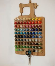 a wooden cutting board with scissors and spools of thread hanging on the wall