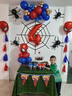 a young boy standing in front of a table with balloons and spiderman decorations on it