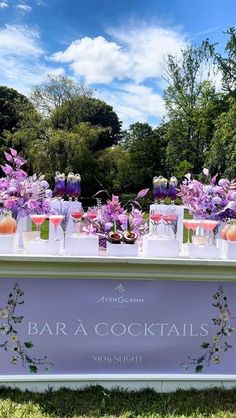 an outdoor bar is decorated with purple flowers and wine glasses for cocktails on the table