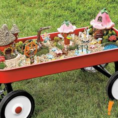 a red wagon filled with lots of toys on top of a grass covered field next to trees