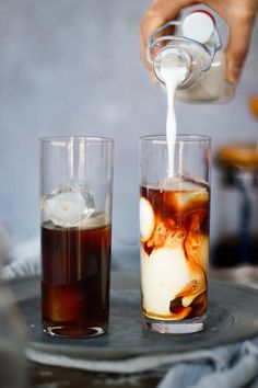 two glasses filled with liquid and ice being poured into one glass while another is on the other side