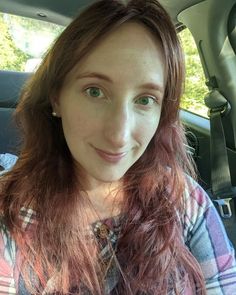 a woman sitting in the back seat of a car with long red hair and green eyes