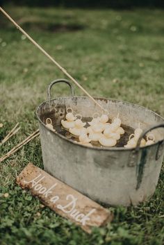 a metal bucket filled with mushrooms sitting on top of a lush green field next to a wooden sign