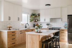 a kitchen with white cabinets and wooden floors is pictured in this image, there are four stools at the center of the island