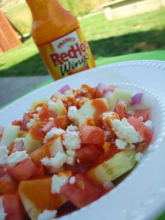 a white plate topped with fruit and feta cheese next to a bottle of orange juice