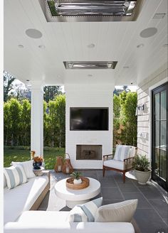 an outdoor living area with white furniture and a flat screen tv mounted above the fireplace