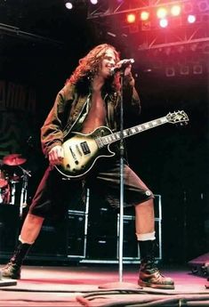 a man with long hair playing guitar on stage