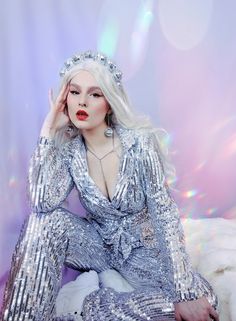 a woman with long white hair sitting on top of a bed wearing silver sequins