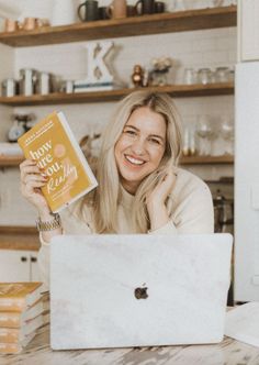 a woman sitting at a table with a laptop and book in front of her face