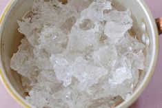 a bowl filled with ice sitting on top of a pink table next to a bottle