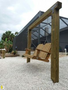 a wooden swing sitting in the middle of a gravel covered area next to a building