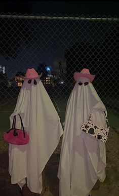 two white ghost costumes with pink hats and purses on their heads are standing in front of a chain link fence