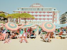 many people are sitting on the beach with umbrellas and chairs in front of them