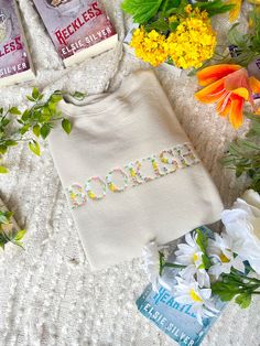 some flowers and books are laying on a bed with a white sweater that says rockin '