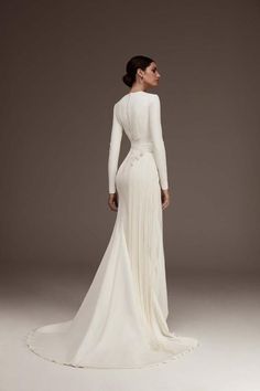 a woman in a white wedding dress with long sleeves and an open back, standing on a