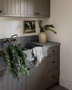 a kitchen with gray cabinets and plants on the counter top, along with a white checkered dish towel