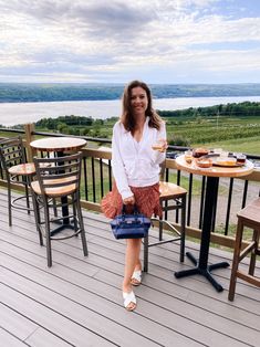 a woman standing on a deck holding a blue purse and smiling at the camera,