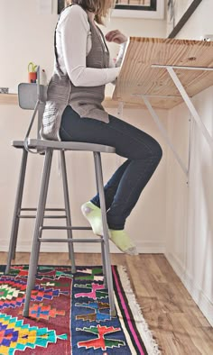 a woman sitting at a table using a laptop computer on top of a wooden stool