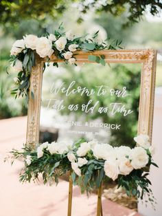 a sign that says welcome to our guests at the end of their wedding ceremony with white flowers and greenery