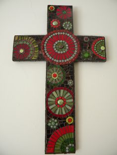 a cross made out of stained glass with flowers and circles on the bottom, sitting against a white wall