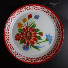 a red and white plate with flowers painted on the side, sitting on a table