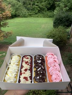 an open box filled with assorted donuts on top of a lush green field