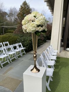 a vase filled with white and pink flowers on top of a pedestal next to chairs