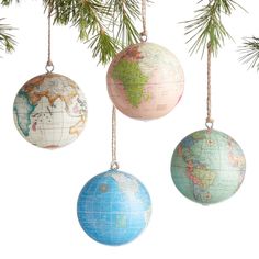 three ornaments hanging from a christmas tree with the world map on one ornament