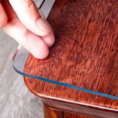 a hand is touching the edge of a wooden table with a clear glass strip on it