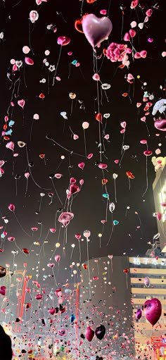 many balloons are floating in the air with hearts on them and people standing under them