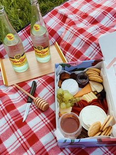 an open box of cheese and crackers on a picnic blanket with two bottles of wine in the background