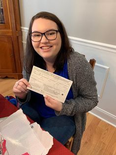 a woman sitting on the floor holding up a cheque paper with an envelope in front of her