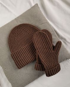 two knitted mittens sitting on top of a pillow next to a gray pillow