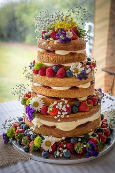 a multi layer cake with fresh fruit and flowers on top is sitting on a table