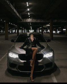 a woman sitting on the hood of a car in a parking garage with her legs crossed