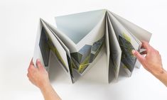 two hands are holding an open book that is folded in half and has pictures on it