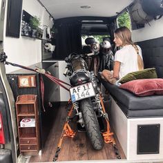 two people sitting in the back of a van with a motorcycle parked next to them