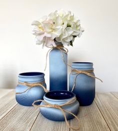 three blue vases with white flowers in them on a wooden table next to each other