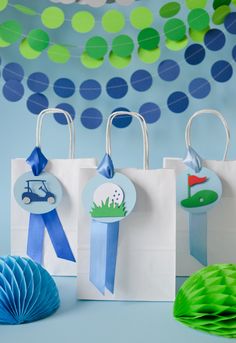 three paper bags with blue ribbon and golf themed tags on them, sitting next to some decorations