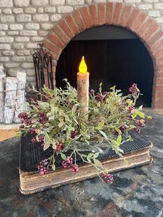 a lit candle is sitting on top of an old book with berries and leaves in front of a brick fireplace