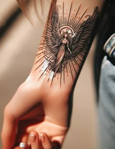 a woman's arm with an angel tattoo on it, holding her hand up to the camera