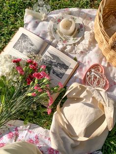 an open book sitting on top of a grass covered field next to flowers and a basket