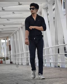 a man in black shirt and jeans walking down a walkway with sunglasses on his head