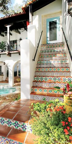 an outdoor swimming pool next to a white house with colorful tiles on the steps leading up to it