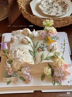 a cake decorated with flowers on top of a wooden table next to a wicker basket